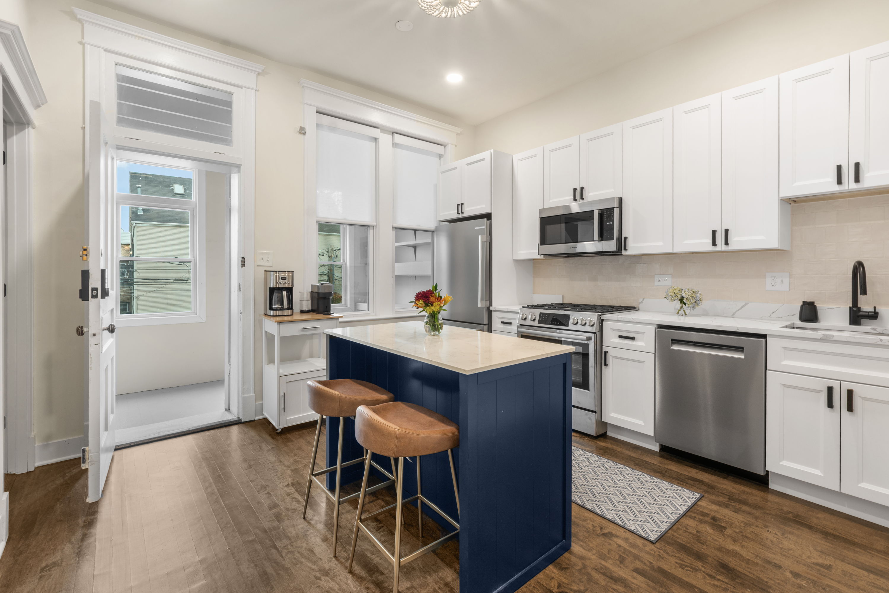 Kitchen with a navy island, leather stools, white shaker cabinets, and stainless appliances